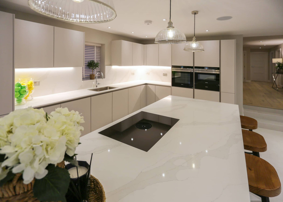 Photo of a large scandinavian single-wall open plan kitchen in Hertfordshire with a single-bowl sink, flat-panel cabinets, white cabinets, quartzite benchtops, white splashback, black appliances, with island, white floor and white benchtop.