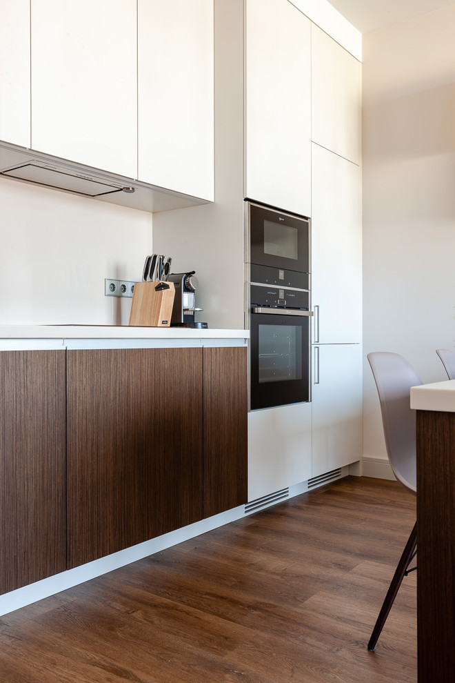 This is an example of a mid-sized contemporary single-wall open plan kitchen in Moscow with a drop-in sink, flat-panel cabinets, beige cabinets, quartzite benchtops, beige splashback, stone slab splashback, black appliances, medium hardwood floors, with island, brown floor and beige benchtop.