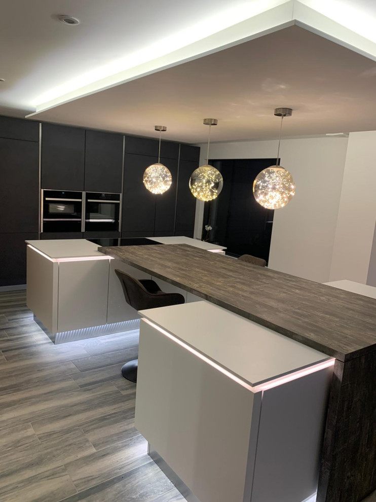 Large modern u-shaped eat-in kitchen in London with flat-panel cabinets, grey cabinets, solid surface benchtops, dark hardwood floors, with island, brown floor and grey benchtop.