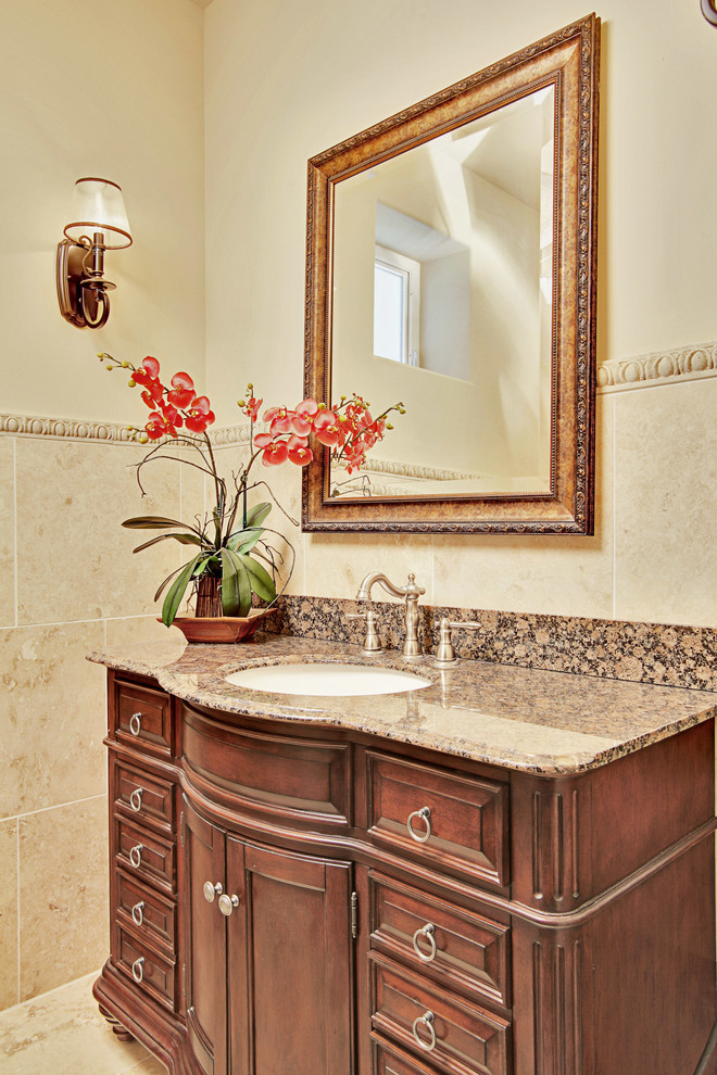 Photo of a mediterranean powder room in Seattle with an undermount sink, furniture-like cabinets, dark wood cabinets, granite benchtops, beige tile, stone tile and beige walls.