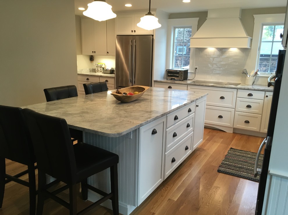 Transitional l-shaped medium tone wood floor eat-in kitchen photo in Boston with a farmhouse sink, shaker cabinets, white cabinets, white backsplash, porcelain backsplash, stainless steel appliances and an island