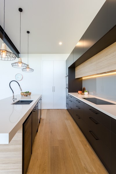 Photo of a scandinavian galley eat-in kitchen in Adelaide with flat-panel cabinets, grey cabinets, marble benchtops, grey splashback, glass sheet splashback, black appliances, light hardwood floors and with island.