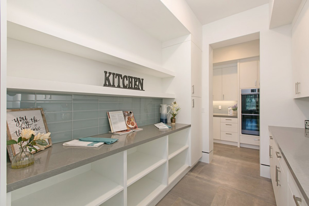 Contemporary galley kitchen pantry in San Diego with a farmhouse sink, flat-panel cabinets, white cabinets, quartzite benchtops, blue splashback, glass tile splashback, black appliances, porcelain floors, with island, grey floor and grey benchtop.