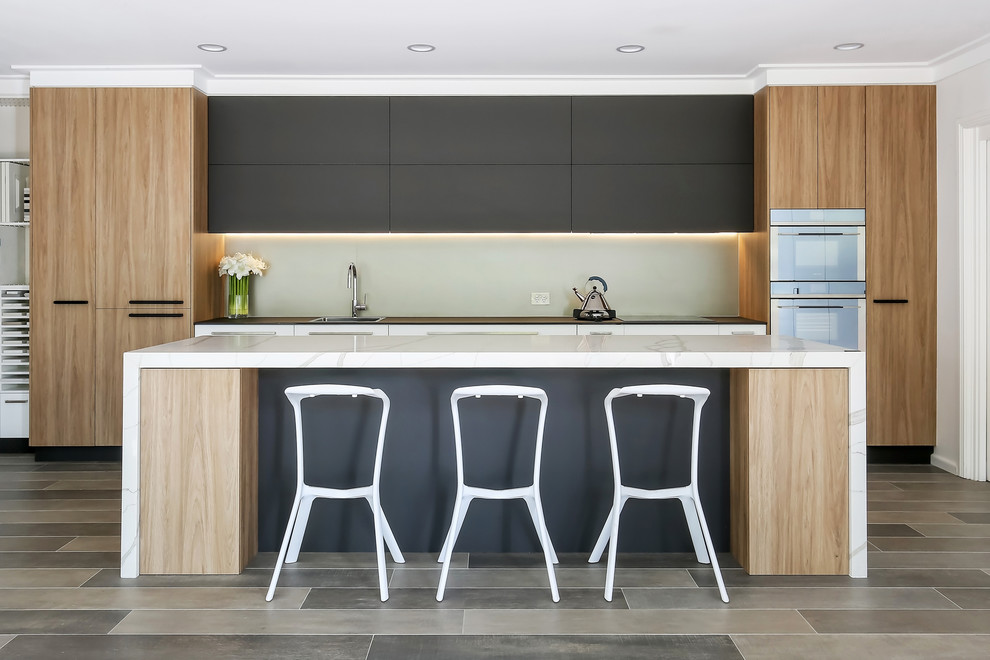 Inspiration for a large contemporary galley open plan kitchen in Sydney with a drop-in sink, flat-panel cabinets, quartz benchtops, porcelain floors, with island, white benchtop, grey cabinets, glass sheet splashback, white appliances and grey floor.