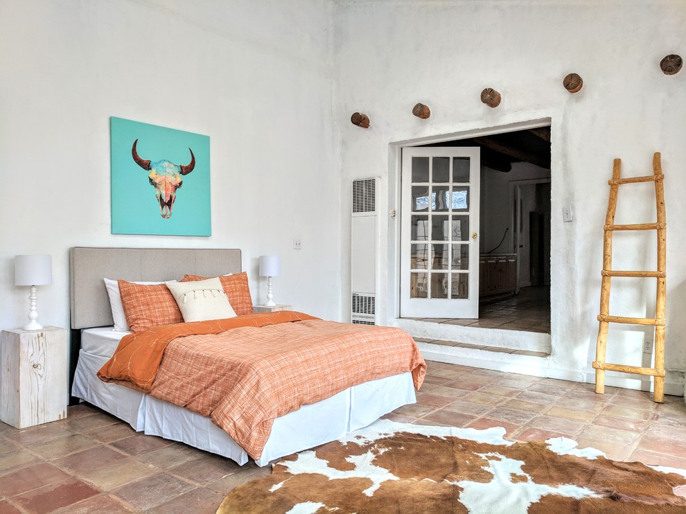 Photo of a large master bedroom in Other with white walls, terra-cotta floors, a corner fireplace, a concrete fireplace surround and beige floor.