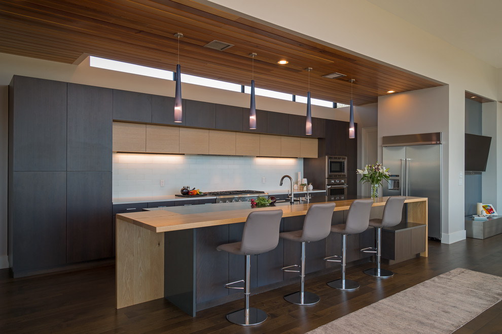 Large contemporary single-wall open plan kitchen in Austin with flat-panel cabinets, quartz benchtops, stainless steel appliances, medium hardwood floors, with island, black cabinets, brown floor, a drop-in sink, white splashback, ceramic splashback and beige benchtop.