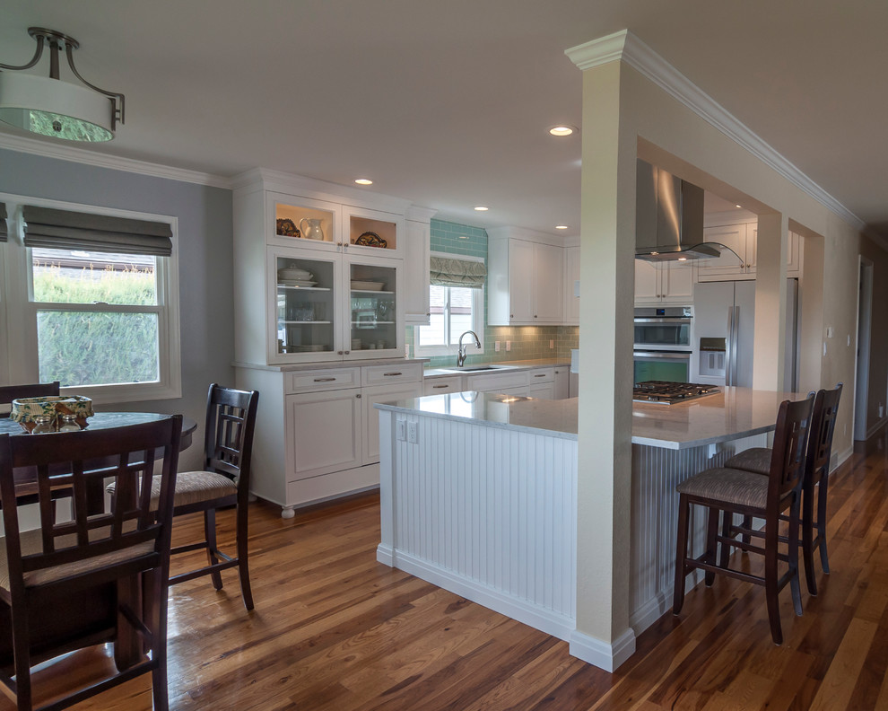 Example of a mid-sized transitional medium tone wood floor eat-in kitchen design in Denver with a single-bowl sink, flat-panel cabinets, yellow cabinets, quartz countertops, blue backsplash, glass tile backsplash, white appliances and an island