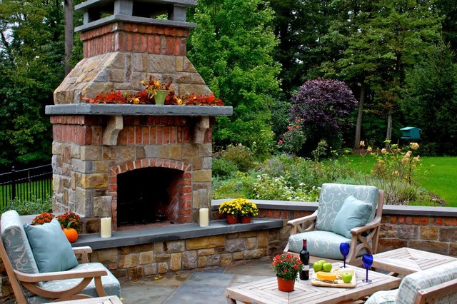 This bluestone patio living space is anchored by a stone fireplace that incorporates brick to tie it back to the brick residence.  This fireplace extends the