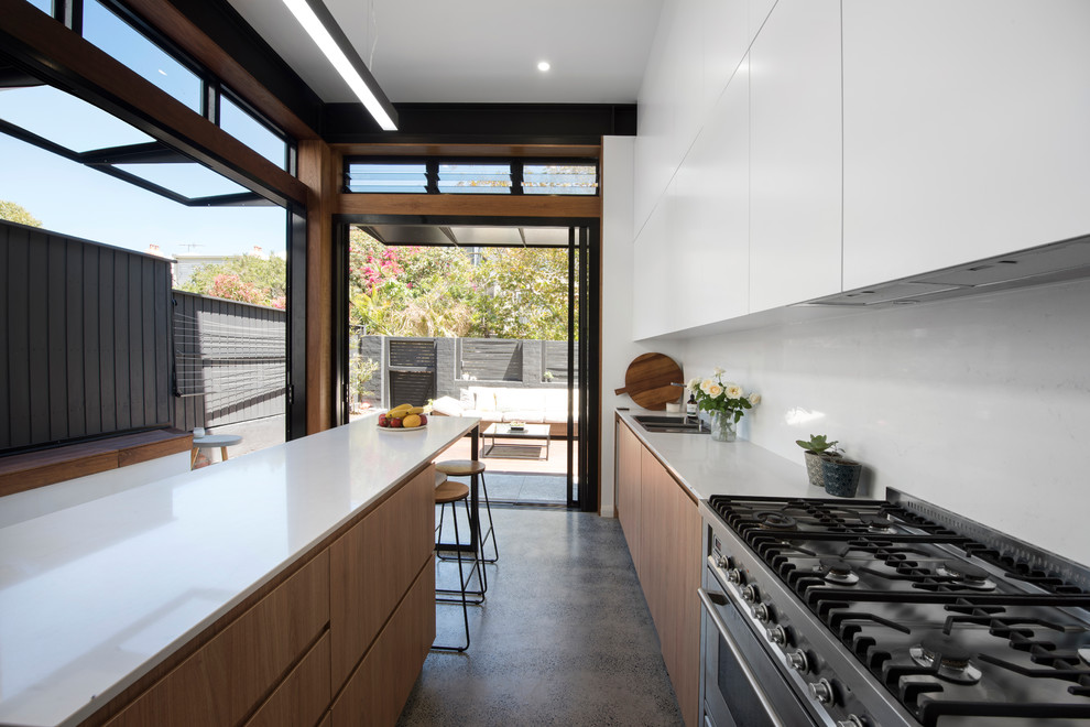 This is an example of a mid-sized modern single-wall eat-in kitchen in Newcastle - Maitland with a double-bowl sink, flat-panel cabinets, white cabinets, white splashback, stainless steel appliances, concrete floors, with island, grey floor and white benchtop.