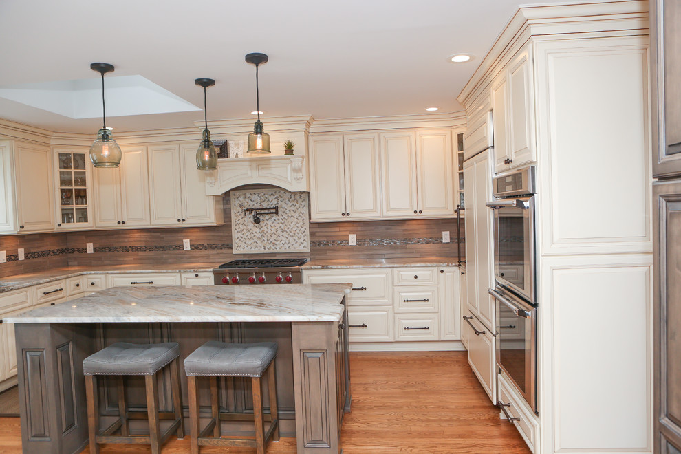 Eat-in kitchen - large transitional u-shaped light wood floor eat-in kitchen idea in Newark with an undermount sink, raised-panel cabinets, distressed cabinets, granite countertops, brown backsplash, mosaic tile backsplash, stainless steel appliances and an island