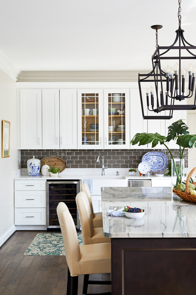 Example of a transitional brown floor kitchen design in DC Metro with an undermount sink, shaker cabinets, white cabinets, gray backsplash, stainless steel appliances, an island and white countertops