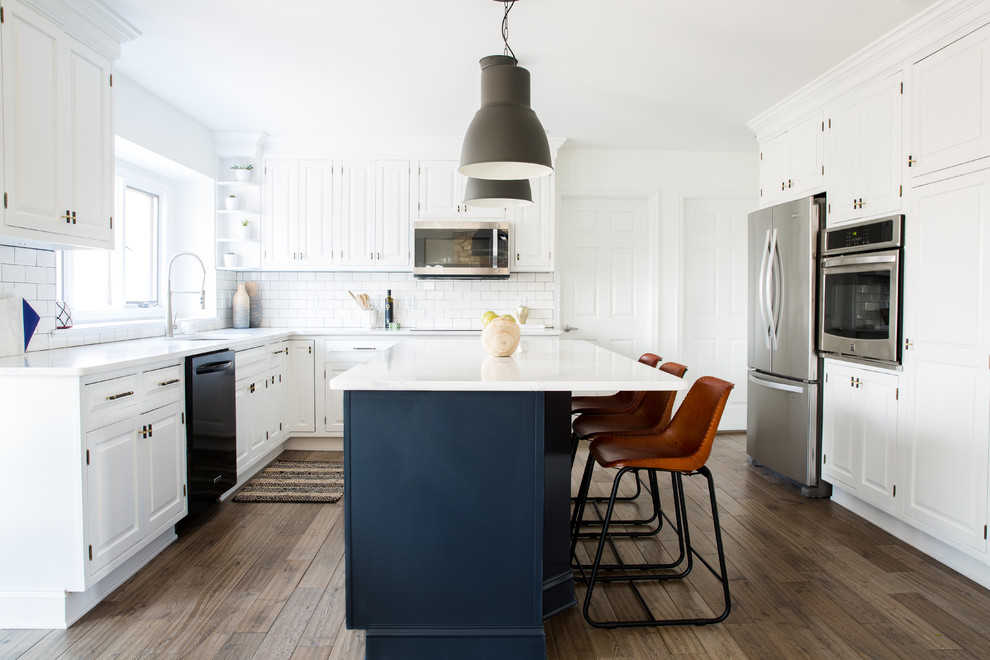 Example of a transitional l-shaped medium tone wood floor kitchen design in Los Angeles with white cabinets, marble countertops, white backsplash, subway tile backsplash, stainless steel appliances, an island, an undermount sink and raised-panel cabinets