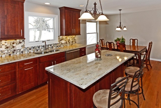 Mid-sized transitional l-shaped medium tone wood floor eat-in kitchen photo in Chicago with an undermount sink, recessed-panel cabinets, medium tone wood cabinets, granite countertops, gray backsplash, glass tile backsplash, stainless steel appliances, beige walls and an island