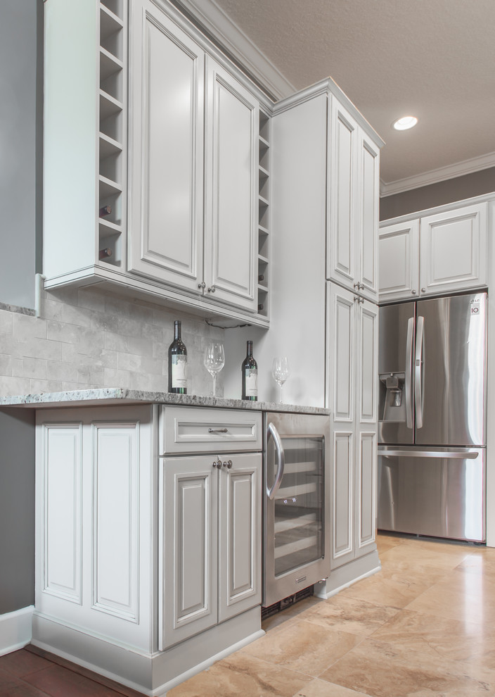 Inspiration for a mid-sized contemporary l-shaped eat-in kitchen in Jacksonville with a farmhouse sink, raised-panel cabinets, white cabinets, granite benchtops, beige splashback, stainless steel appliances and with island.