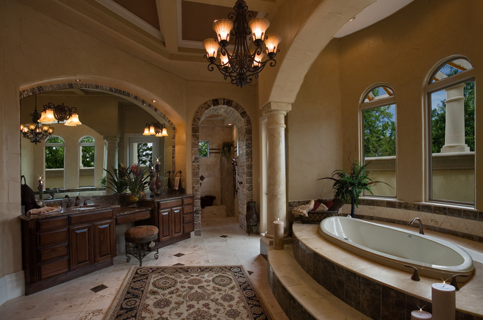 Expansive mediterranean master bathroom in Miami with an undermount sink, raised-panel cabinets, dark wood cabinets, granite benchtops, a drop-in tub, a curbless shower, beige tile, stone tile, beige walls and travertine floors.
