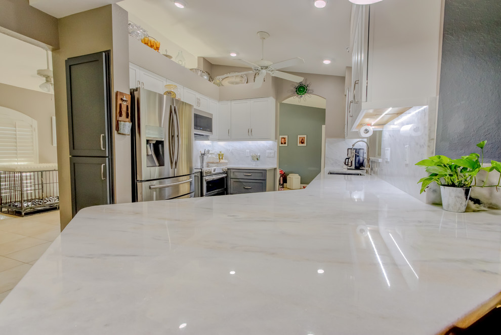 Mid-sized trendy galley home design photo with an undermount sink, shaker cabinets, white cabinets, quartz countertops, white backsplash, stone slab backsplash, stainless steel appliances, a peninsula and white countertops