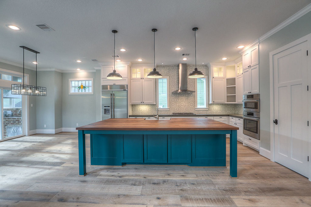 Design ideas for a large transitional l-shaped open plan kitchen in Orange County with a farmhouse sink, shaker cabinets, white cabinets, granite benchtops, grey splashback, ceramic splashback, stainless steel appliances, light hardwood floors and with island.