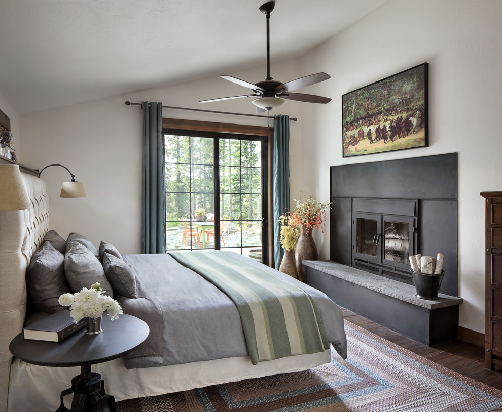 Country master bedroom in Other with white walls, dark hardwood floors, a standard fireplace, a metal fireplace surround and brown floor.