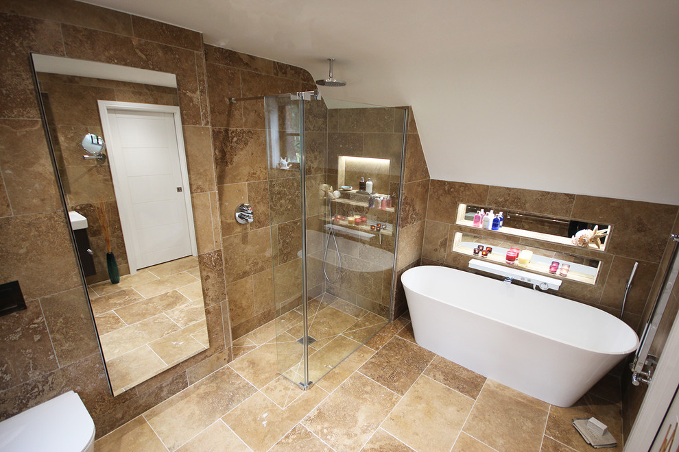 Large contemporary master bathroom in Surrey with flat-panel cabinets, brown cabinets, a freestanding tub, an open shower, a wall-mount toilet, brown tile, travertine, brown walls, travertine floors, an integrated sink and brown floor.