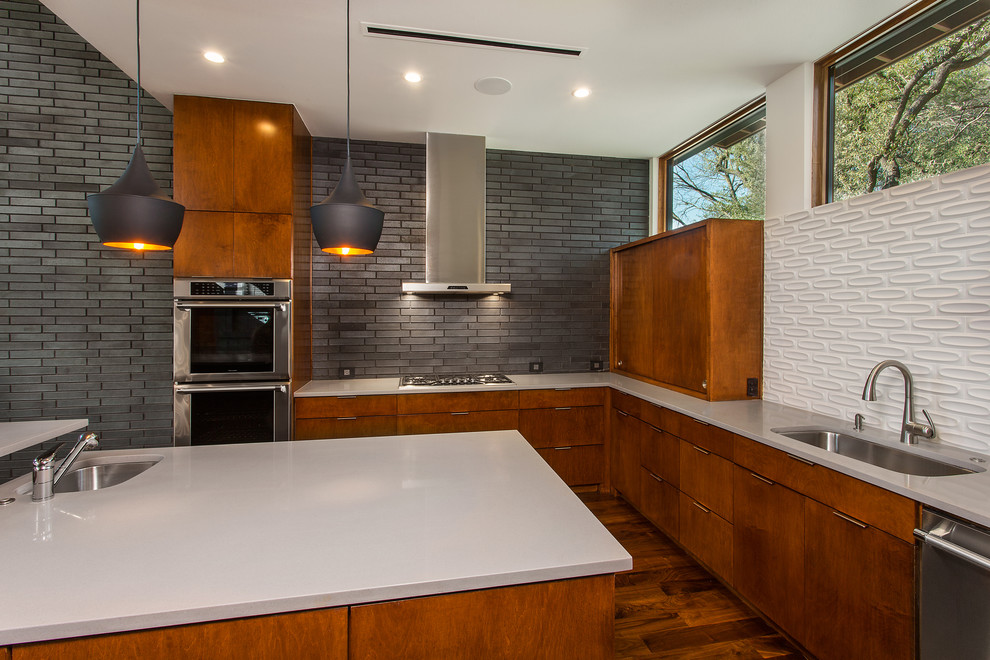 Mid-sized midcentury u-shaped open plan kitchen in Dallas with an undermount sink, flat-panel cabinets, medium wood cabinets, solid surface benchtops, white splashback, ceramic splashback, stainless steel appliances, dark hardwood floors, with island and brown floor.