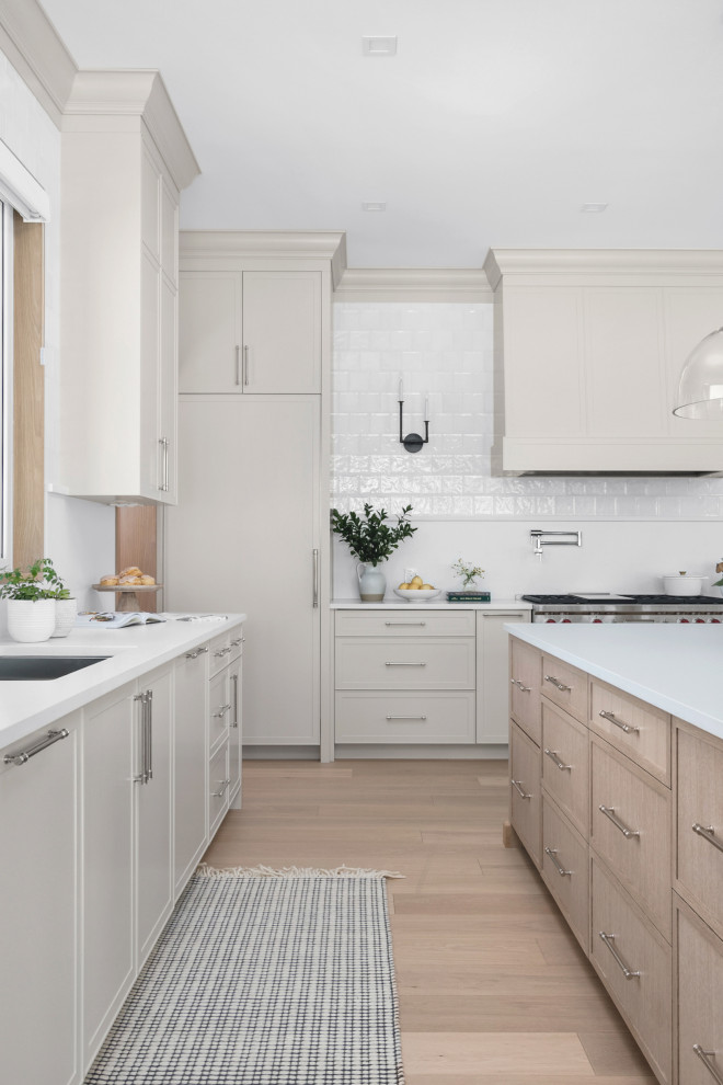 Example of a large transitional l-shaped light wood floor kitchen design with shaker cabinets, quartz countertops, white backsplash, quartz backsplash, stainless steel appliances, an island and white countertops