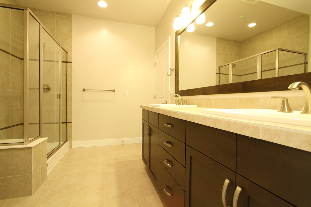 This is an example of a large transitional master bathroom in Denver with a drop-in tub, a corner shower, beige tile, porcelain tile, beige walls, flat-panel cabinets, dark wood cabinets, a drop-in sink, tile benchtops, travertine floors and beige floor.