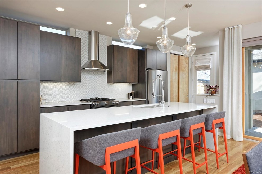This is an example of a contemporary open plan kitchen in Denver with an undermount sink, flat-panel cabinets, dark wood cabinets, white splashback, stainless steel appliances, light hardwood floors, with island, beige floor and white benchtop.