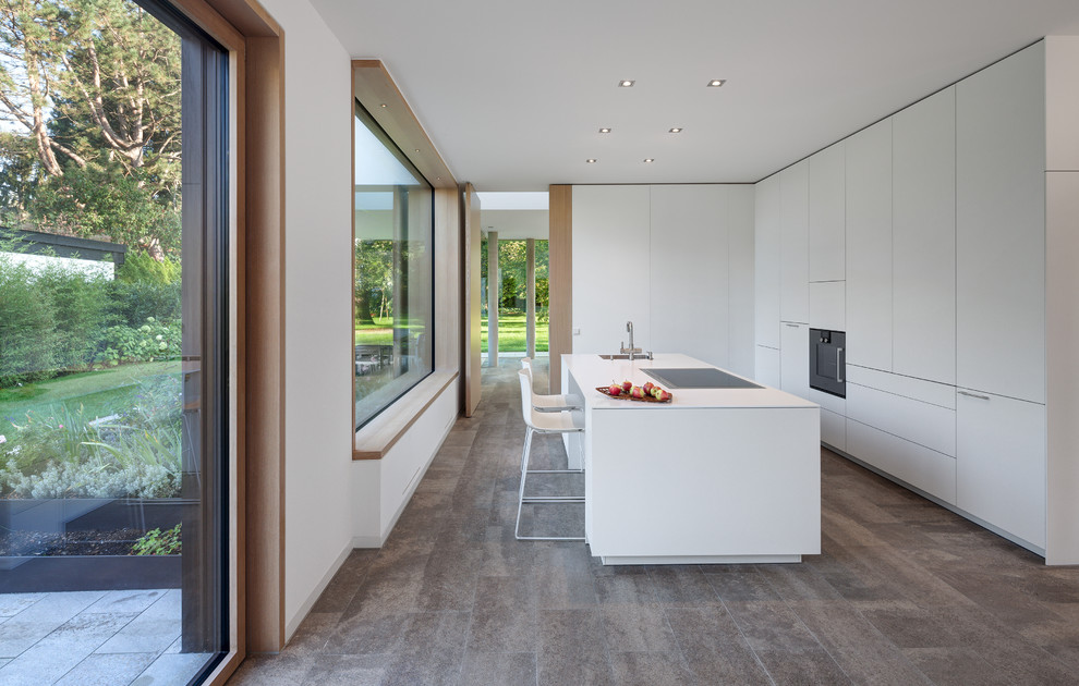 Inspiration for a mid-sized modern separate kitchen in Munich with a single-bowl sink, flat-panel cabinets, white cabinets, solid surface benchtops, limestone floors, with island and black appliances.