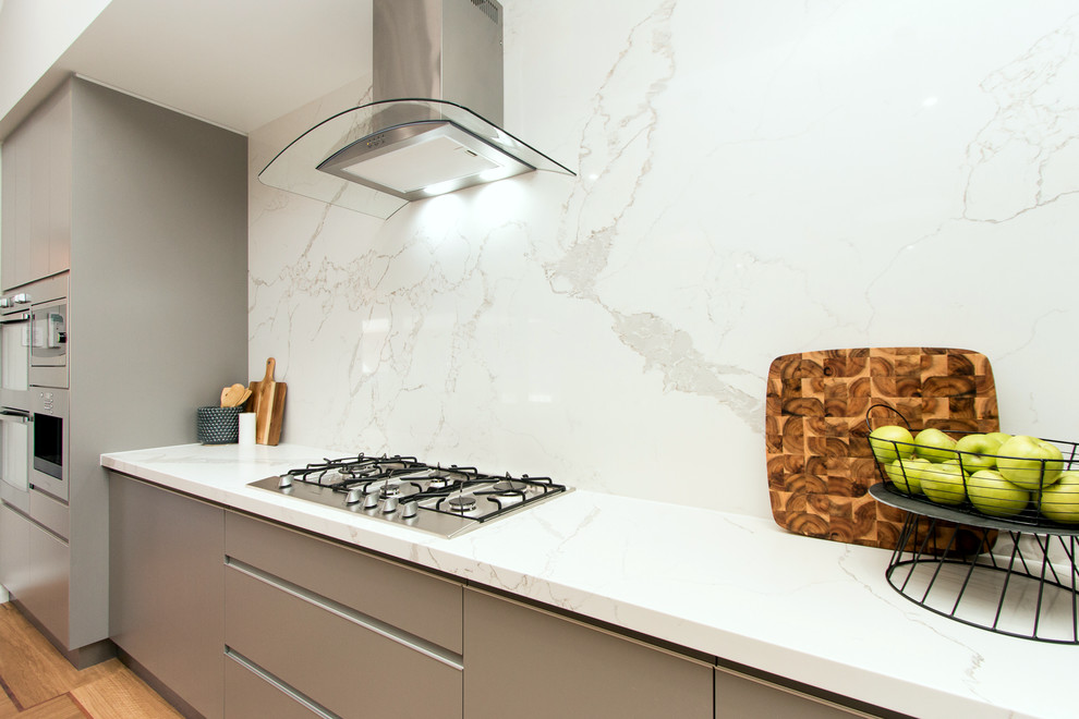 This is an example of a small modern galley open plan kitchen in Perth with quartz benchtops, white splashback, stone slab splashback, with island and white benchtop.