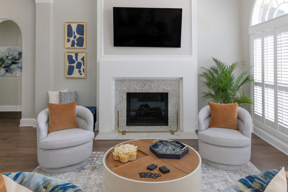 Пример оригинального дизайна: большая открытая гостиная комната в стиле ретро с серыми стенами, паркетным полом среднего тона, двусторонним камином, фасадом камина из дерева, телевизором на стене и коричневым полом
