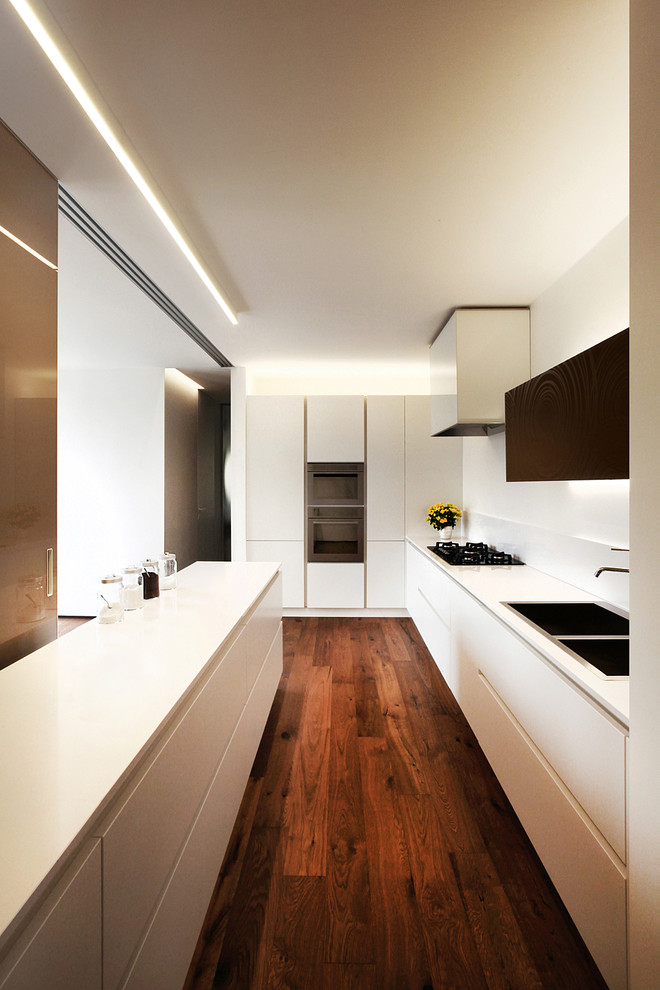 Design ideas for a large contemporary l-shaped open plan kitchen in Venice with an integrated sink, flat-panel cabinets, white cabinets, solid surface benchtops, white splashback, stainless steel appliances, a peninsula and dark hardwood floors.