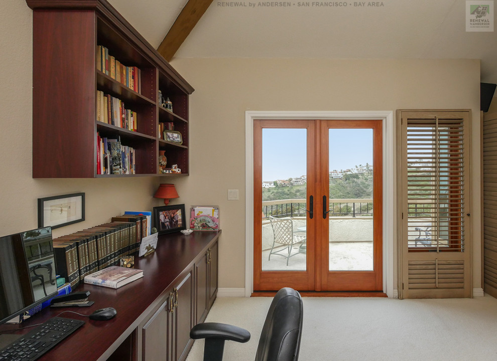 Imagen de despacho de tamaño medio con paredes beige, moqueta, chimenea de doble cara, escritorio empotrado, suelo beige y vigas vistas