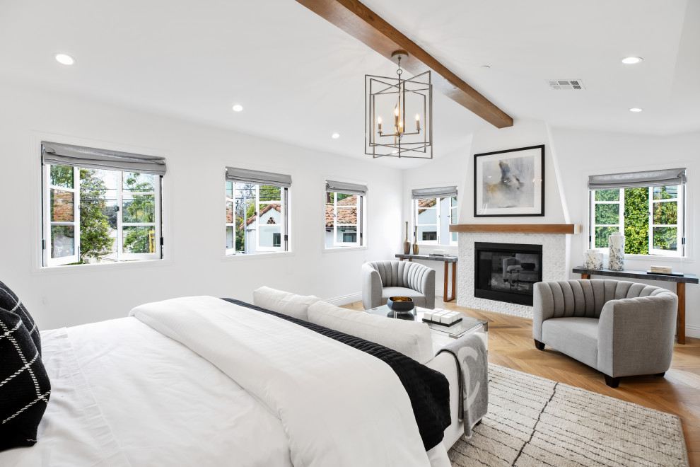 Design ideas for a transitional bedroom in Los Angeles with white walls, medium hardwood floors, a standard fireplace, brown floor, exposed beam and vaulted.