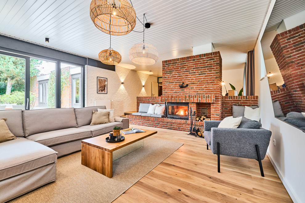 Photo of a scandinavian open plan living room in Other with a wood burning stove, a brick fireplace surround, a wall mounted tv, a timber clad ceiling, white walls, light hardwood flooring, beige floors and brick walls.