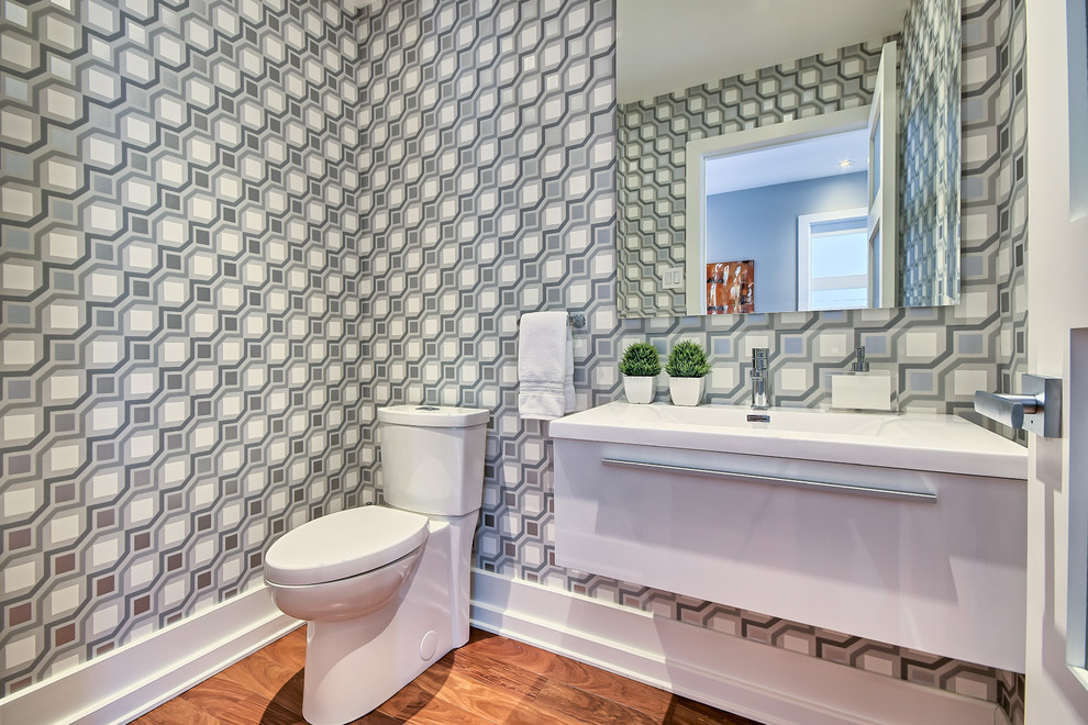 Small contemporary powder room in Montreal with flat-panel cabinets, white cabinets, a two-piece toilet, grey walls, medium hardwood floors and an integrated sink.