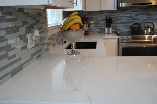 Modern white kitchen with quartz countertop, glass tile backsplash and white kitchen cabinets, featuring a fruit bowl centerpiece