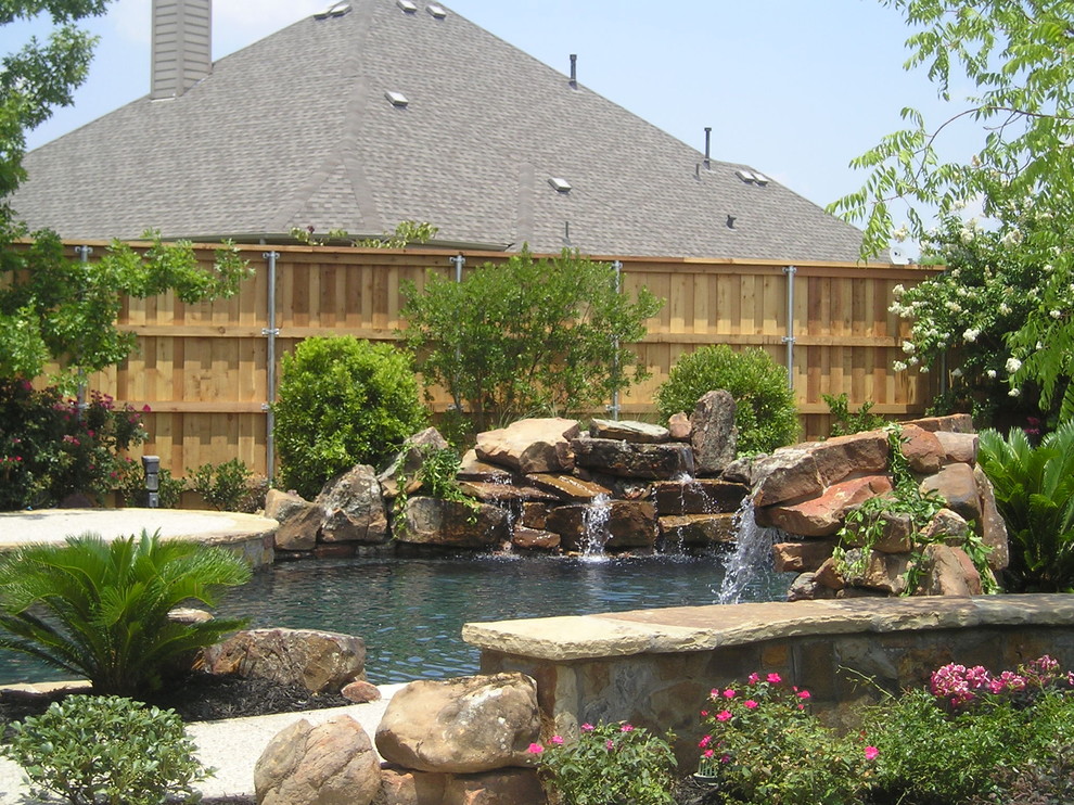 Design ideas for a large arts and crafts backyard custom-shaped natural pool in Dallas with a water feature and concrete slab.