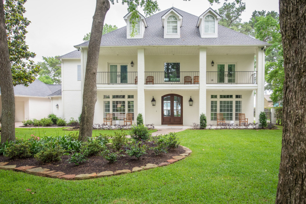 Photo of a large beach style two-storey white house exterior in Houston with painted brick siding and a shingle roof.