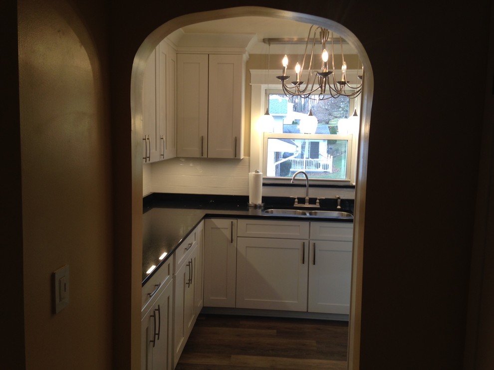 Example of a mid-sized arts and crafts u-shaped vinyl floor home design design with a double-bowl sink, shaker cabinets, white cabinets, quartz countertops, white backsplash, porcelain backsplash, stainless steel appliances and no island