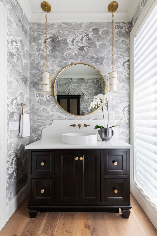 Design ideas for a transitional powder room in Portland with shaker cabinets, brown cabinets, multi-coloured walls, medium hardwood floors, a vessel sink, white benchtops, a freestanding vanity and wallpaper.