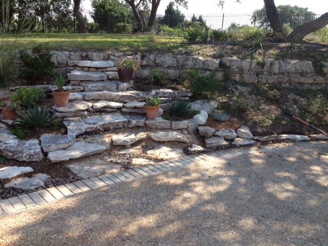 Design ideas for a small sloped partial sun xeriscape for summer in Austin with a retaining wall and natural stone pavers.