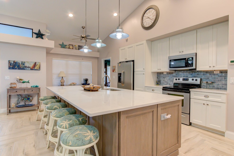 Large single-wall porcelain tile and white floor open concept kitchen photo with an undermount sink, shaker cabinets, white cabinets, quartz countertops, blue backsplash, stainless steel appliances, an island and white countertops