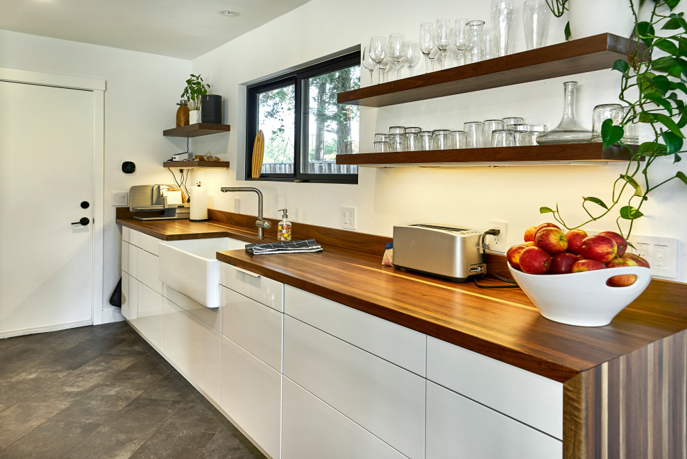 This is an example of a medium sized midcentury l-shaped kitchen/diner in San Francisco with a belfast sink, flat-panel cabinets, medium wood cabinets, wood worktops, brown splashback, wood splashback, integrated appliances, porcelain flooring, an island, grey floors, white worktops and a vaulted ceiling.
