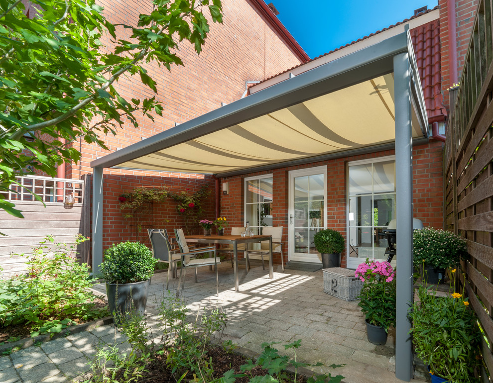 Photo of a traditional backyard patio in Hamburg with a container garden, brick pavers and an awning.