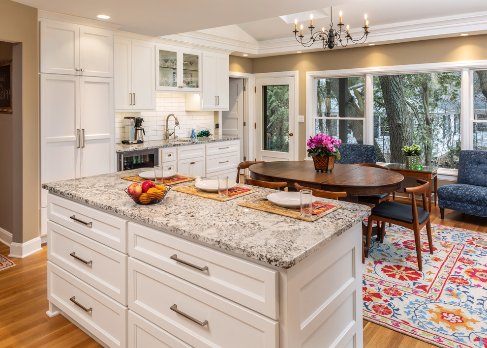 Transitional medium tone wood floor and brown floor eat-in kitchen photo in Milwaukee with a farmhouse sink, shaker cabinets, white cabinets, granite countertops, red backsplash, ceramic backsplash, stainless steel appliances, two islands and white countertops