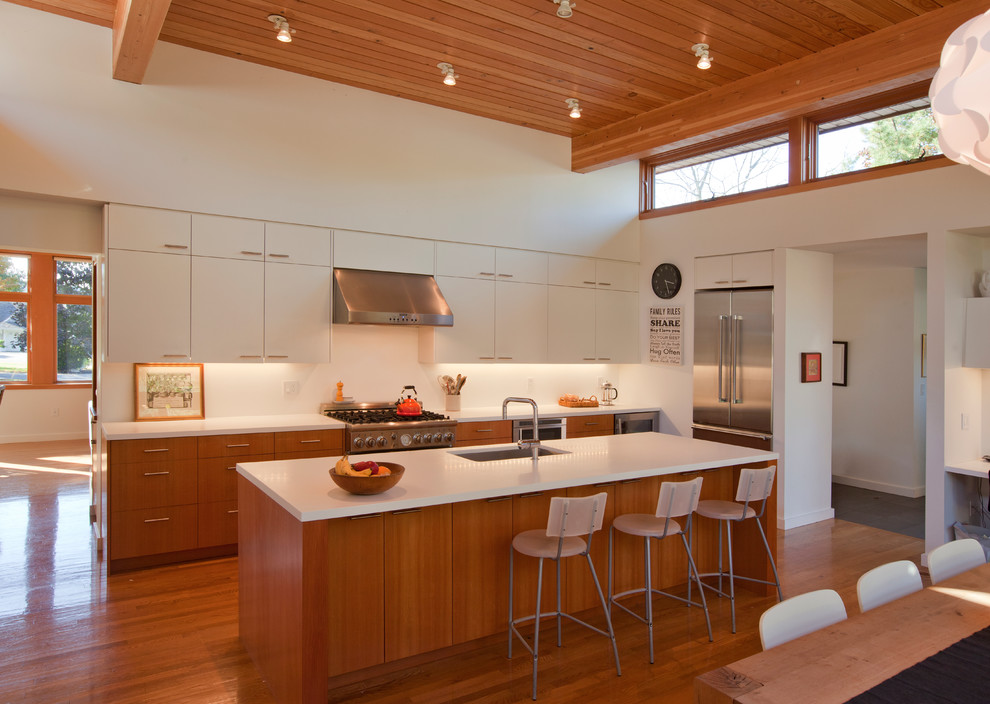 Mid-sized modern l-shaped eat-in kitchen in Boston with a single-bowl sink, flat-panel cabinets, white cabinets, solid surface benchtops, stainless steel appliances, dark hardwood floors, with island and brown floor.