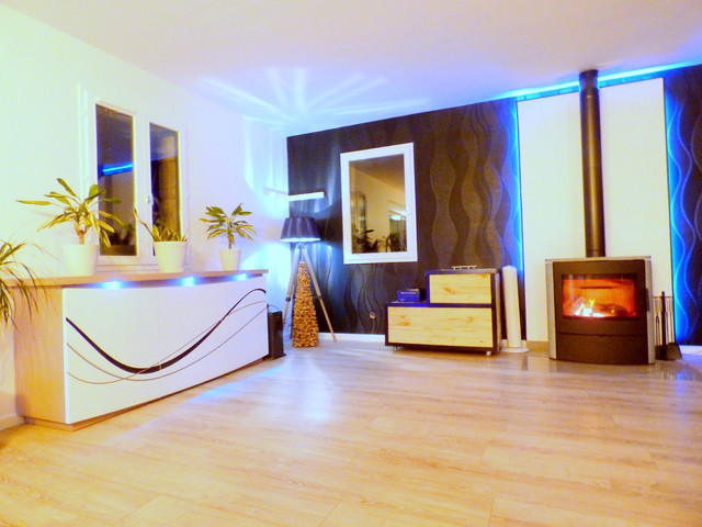 Aménagement d'un très grand salon moderne ouvert avec un mur noir, sol en stratifié, un poêle à bois, un téléviseur indépendant et un sol gris.