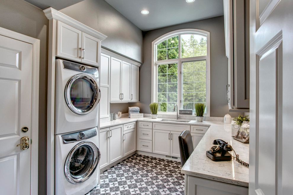 This is an example of a mid-sized contemporary u-shaped utility room in Seattle with an undermount sink, recessed-panel cabinets, white cabinets, quartzite benchtops, grey walls, porcelain floors, a stacked washer and dryer, grey floor and white benchtop.