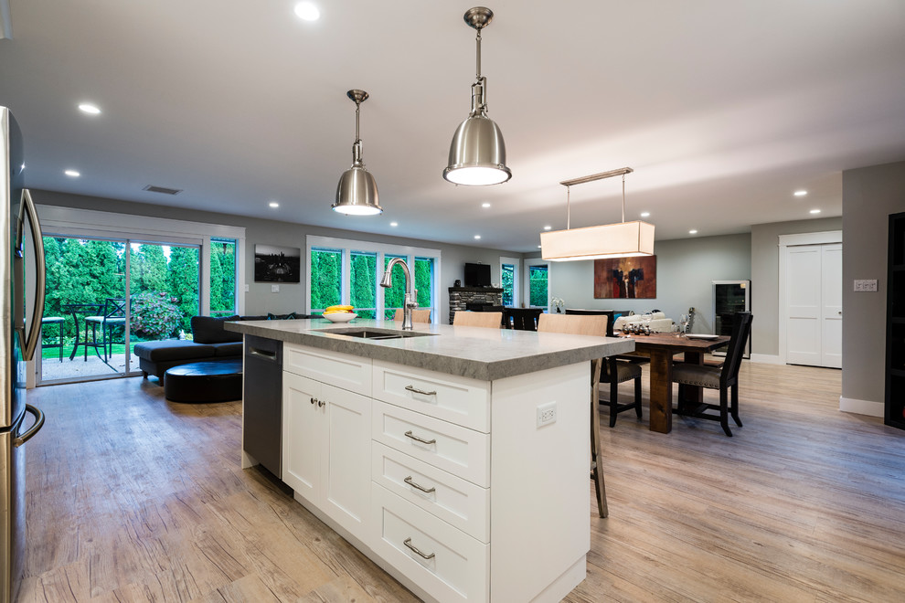 Design ideas for a mid-sized transitional l-shaped open plan kitchen in Vancouver with an undermount sink, raised-panel cabinets, white cabinets, quartz benchtops, grey splashback, porcelain splashback, stainless steel appliances, light hardwood floors, with island and beige floor.