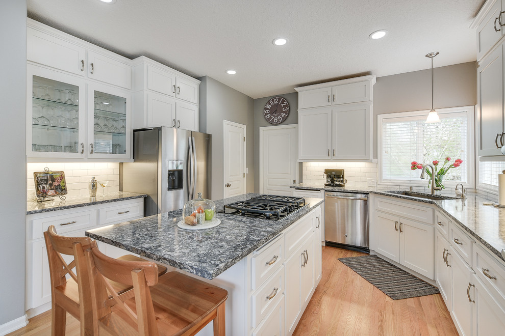 Mid-sized transitional l-shaped light wood floor and brown floor enclosed kitchen photo in Portland with a drop-in sink, shaker cabinets, white cabinets, quartz countertops, white backsplash, subway tile backsplash, an island and stainless steel appliances